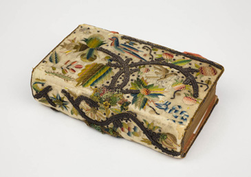 This small bible is covered in silk and intricate embroidery. Brightly coloured plants, birds and other animals have been carefully sewn using a mixture of silk and silver thread. It might be an allusion to the Garden of Eden, reflecting the religious text inside. This embroidered cover to the bible is especially high quality, and could be the work of a middling woman or a professional embroiderer. Women were encouraged to occupy themselves with the needle by creating embroidered items such as book covers, clothing and cushions, especially when they had servants who were able to undertake domestic labour for them. Many of the surviving examples are extremely accomplished.<br />
<br />
This pocket bible reflects the sort of personal item that a middling woman might carry with her as a display of her piety and skill. Wealthy members of the middling sort could also buy embroidery pieces made in commercial workshops rather than at home to showcase their wealth, status and taste.