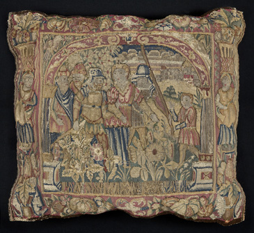 This cushion is linked to the so-called Sheldon tapestry workshop, supposed to have been established in a village in Warwickshire by a man called William Sheldon. In recent years, further research has shown the involvement of immigrant craftspeople in the production, design, and manufacture of the so-called Sheldon tapestries. Indeed, tapestry weaving was not an English skill in the early 1500s. A large number of immigrant weavers came to England in the later sixteenth and early seventeenth centuries, particularly from Flemish areas on the continent. Research suggests that a man called Richard Hyckes was central to the production of these tapestries and to the work of Sheldon and his manufacturing scheme. Hyckes, like many of his colleagues, came to England from the Netherlands, bringing his skill, talent, and experience. He is also connected to the Great Wardrobe in London, part of Elizabeth Is household. She had inherited a large number of extremely valuable tapestries from her father, Henry VIII, for which Hyckes seems to have cared.  <br />
<br />
The ownership of cloths woven with intricate patterns like this one, especially those telling Biblical or classical stories, would have been a prized aesthetic domestic feature for middling and upper-middling individuals  it would have made a clear connection to the much larger pieces in the houses of the nobility and royalty. This cushion is part of a set depicting the story of Susanna and the Elders (in the Old Testament), and shows Susanna, on her way to execution, meeting Daniel, the boy who defended her by speaking up against the Elders slander.Owning sets of matching small domestic textiles is a key feature of upper-middling identity. This object and ones like it stand testament to the skill and labour that came from middling European immigration, and the way it shaped middling domestic life in England.