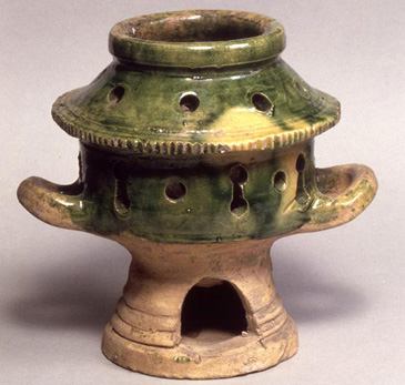 This clay fuming pot is of green and yellow lead glazed Surrey/Hampshire border ware. Fuming pots were used to heat herbs and spices to fragrance and fumigate people's houses. Hot embers would be put inside the pedestal base, which would heat the herbs in the chamber above. The herb chamber has holes in to let the smell of the herbs out. Fuming pots were not only to create pleasant scent. In early modern Europe it was commonly believed that disease spread through miasma (putrid air) so bad smells were a threat to health. Fumigation was therefore a popular method of preventing the spread of the plague. Responsibility for everyday medical practice including both prevention and treatment fell to the mistress of the house, so was a key part of middling womens work. The medical recipe book, <em>A Rich Storehouse</em> OR <em>Treasurie for the Diseased</em> (London, 1612) gives this advice for scenting the home:<br />
<br />
A preservative by correcting the ayre in all houses:<br />
<br />
Take Rosemary dryed, Juniper, Bay-leaves, or Frankincense, and cast the same upon the coles in a chafingdish, and receive the fume or smoke thereof into your head. If you will, put a little Lavender or Sage that is dryed, into the fire with the rest it will do much good. Also to make your fires in eathen pannes (rather to remove about your Chambers, then in Chimneys) shall be better to correct the aires in your houses, then otherwise.<br />
<br />
For middling women, diligence in scenting the home was part of essential domestic tasks and a vital complement to the medical marketplace of apothecaries and physicians.  <br />
<br />
